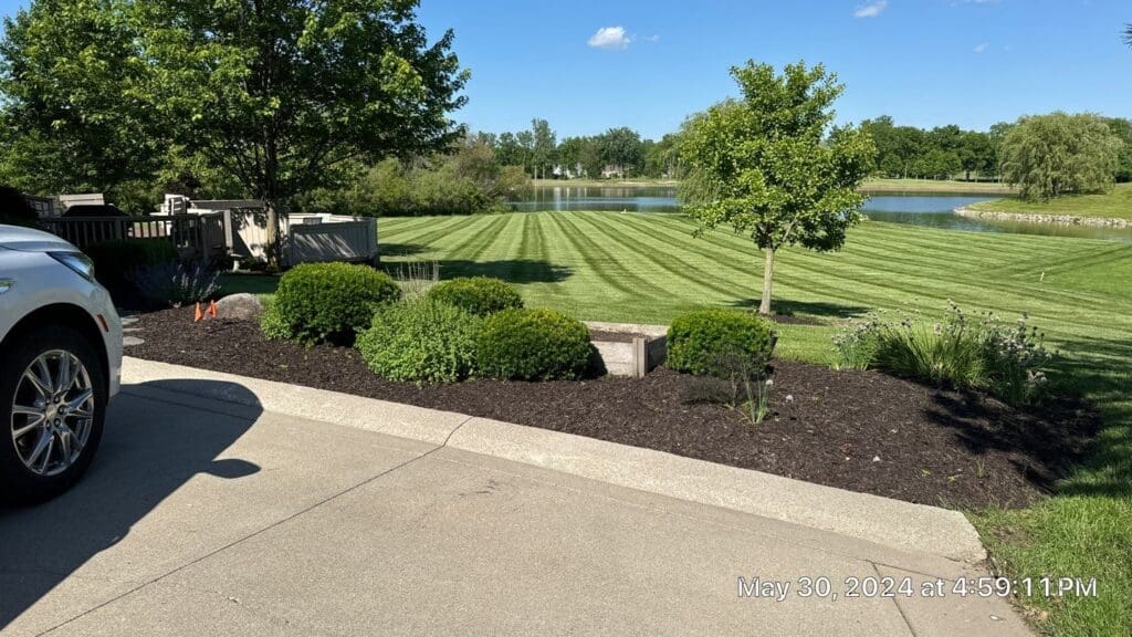 Fort Wayne manicured lawn with mowing stripes, mulched landscaping, shrubs, and pond view.