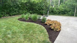 Local Fort Wayne backyard landscaping with curved mulch garden bed, patio, and basketball hoop.