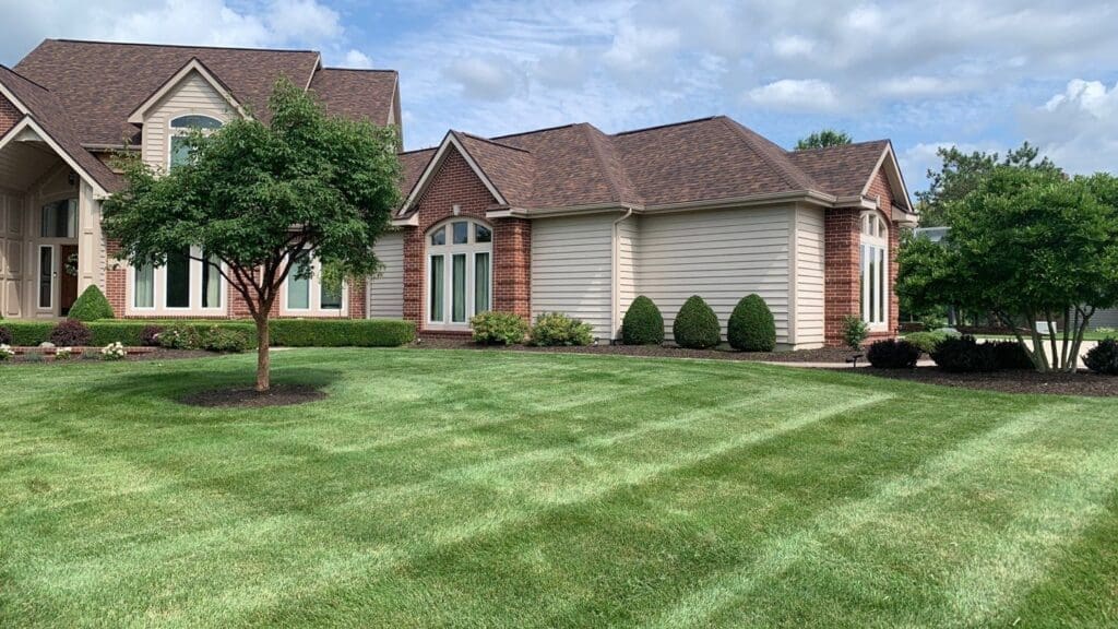 Manicured Fort Wayne suburban lawn with mowing stripes in front of brick home.