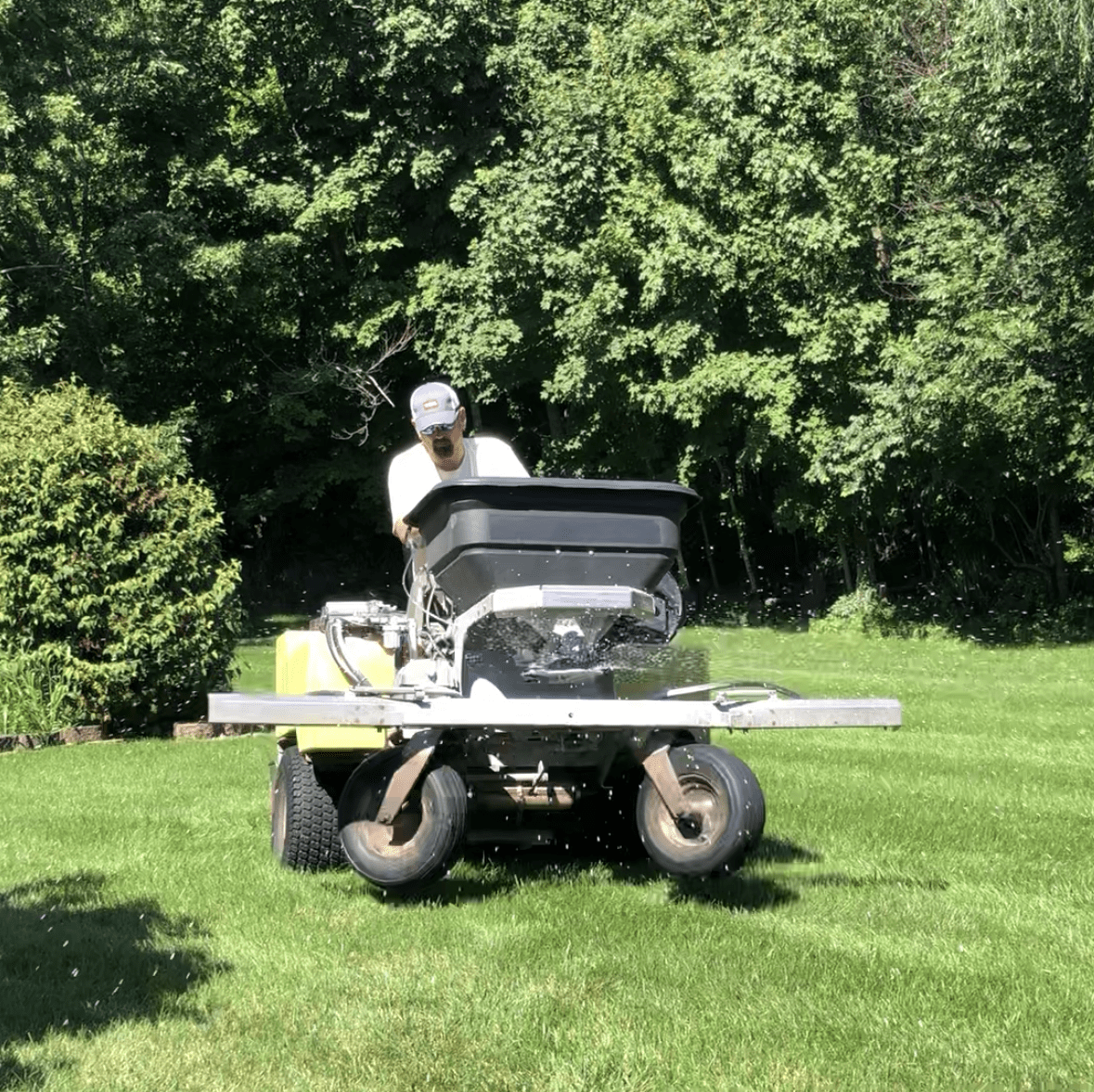 Employee fertilizing a green lawn in Fort Wayne with a ride-on spreader.